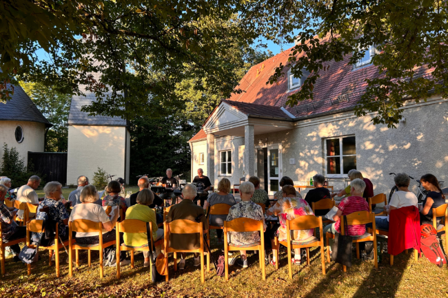 Menschen, die vor dem Gemeindehaus sitzen und gemeinsam singen